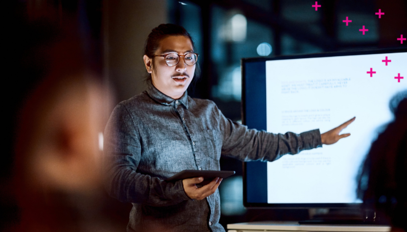 A man holding a tablet points to a tv screen with white writing on it