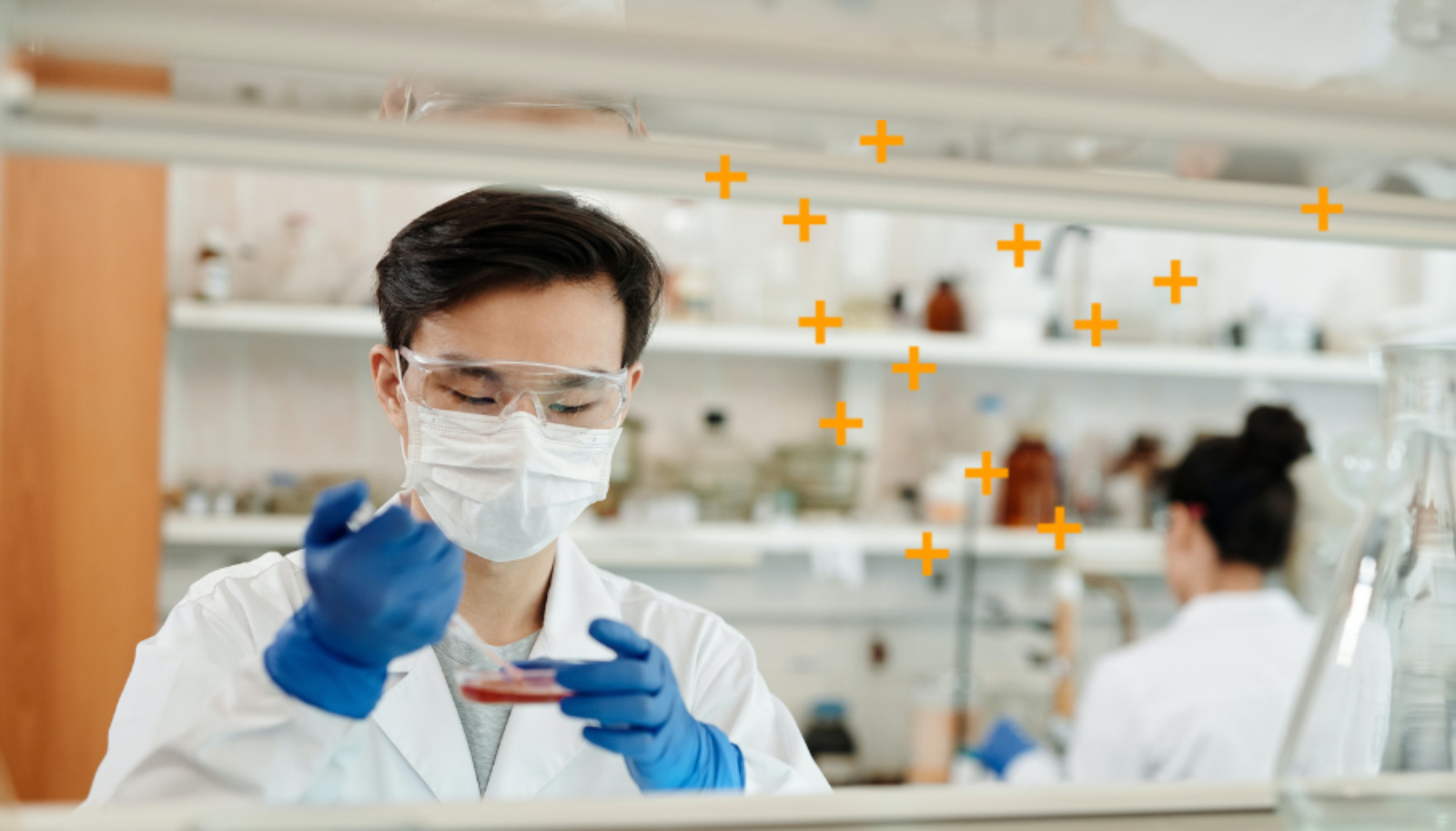 A man holds a petri dish and a syringe in a lab.